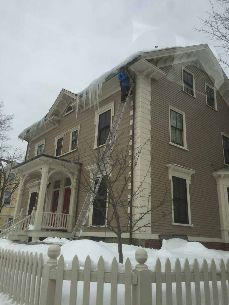 This man is putting himslef in a precarious situation trying to knock off icicles from a house.